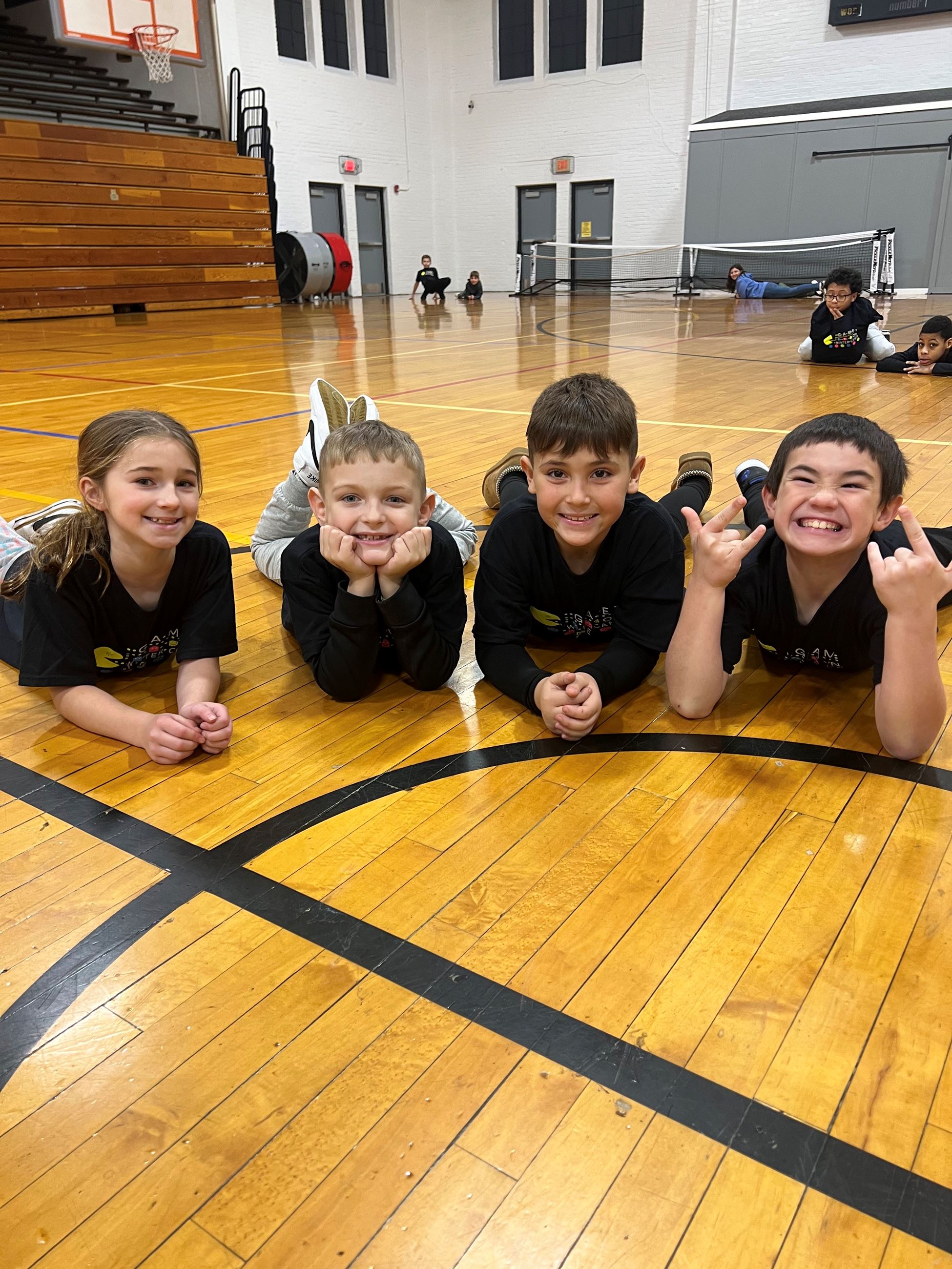 four kids laying on gym floor smiling